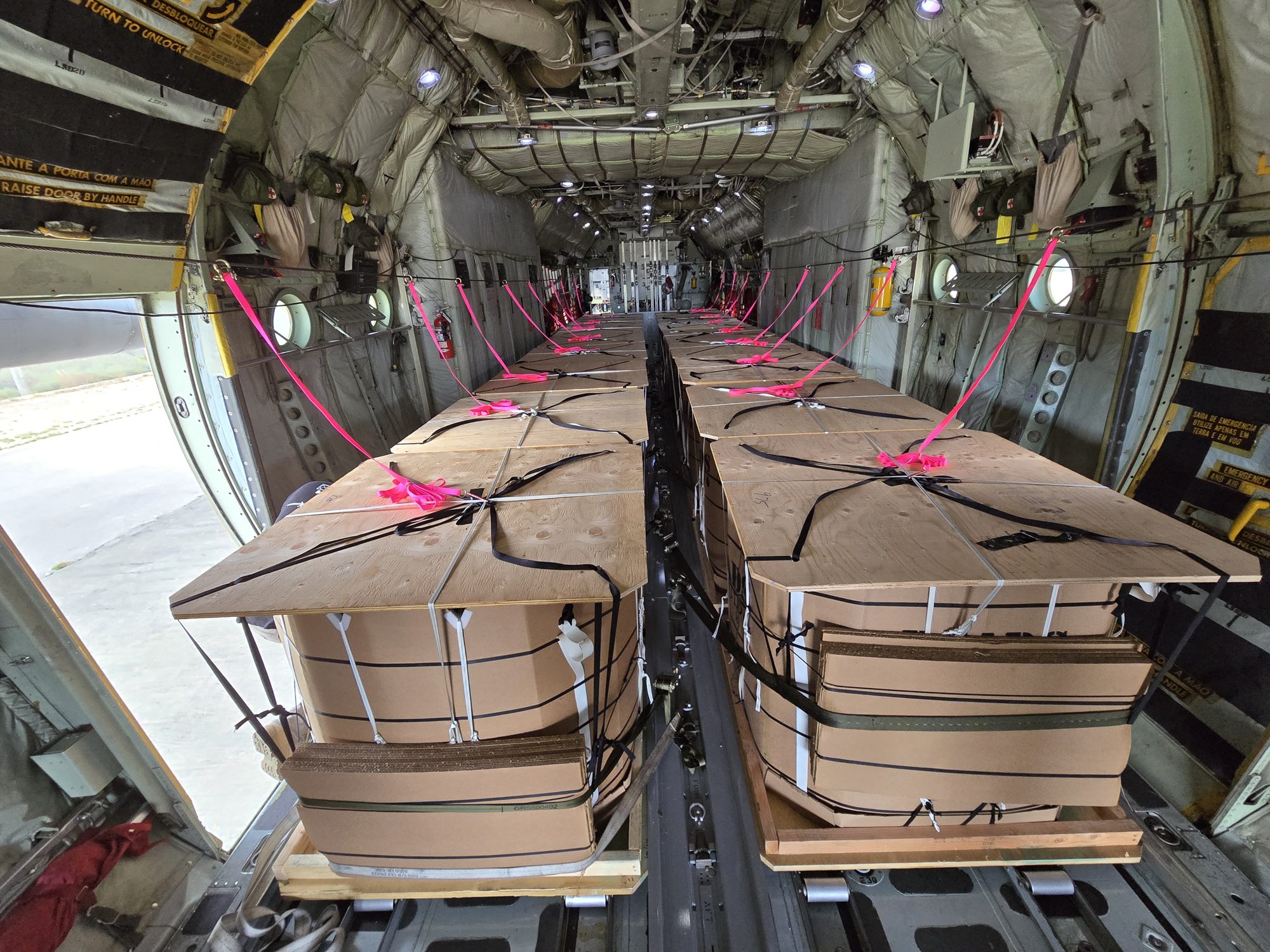 Two rows of PCADS containers tied down on the roller floor inside a C-130 cargo bay