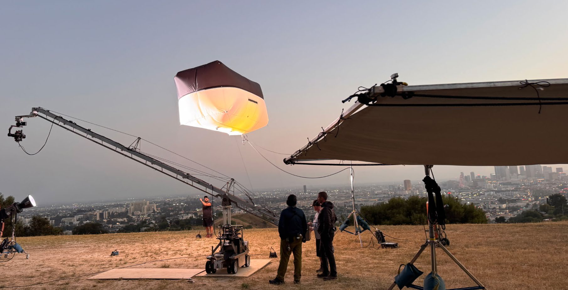 Illuminated lighting balloon suspended from a crane arm over a hillside production at dusk