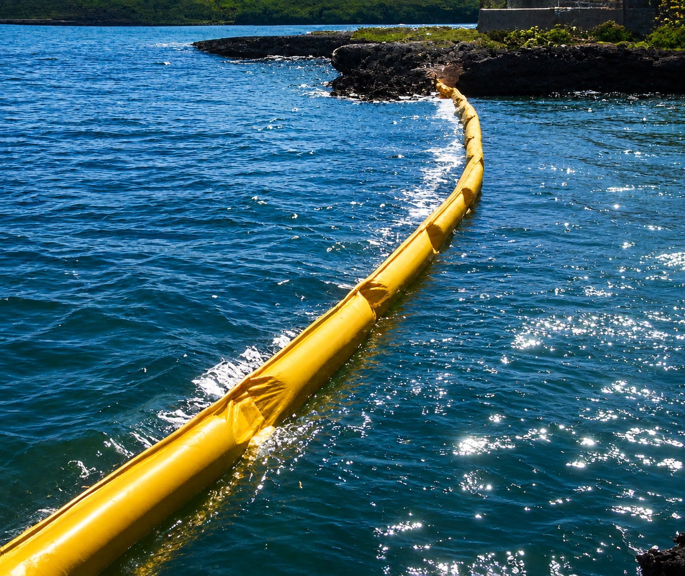Yellow oil containment boom deployed across coastal water toward a rocky shoreline
