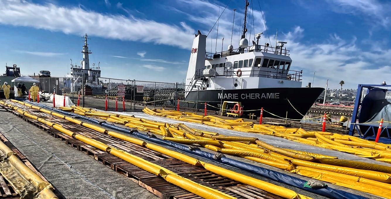 Runs of yellow oil containment boom staged on timber cribbing beside a spill response vessel