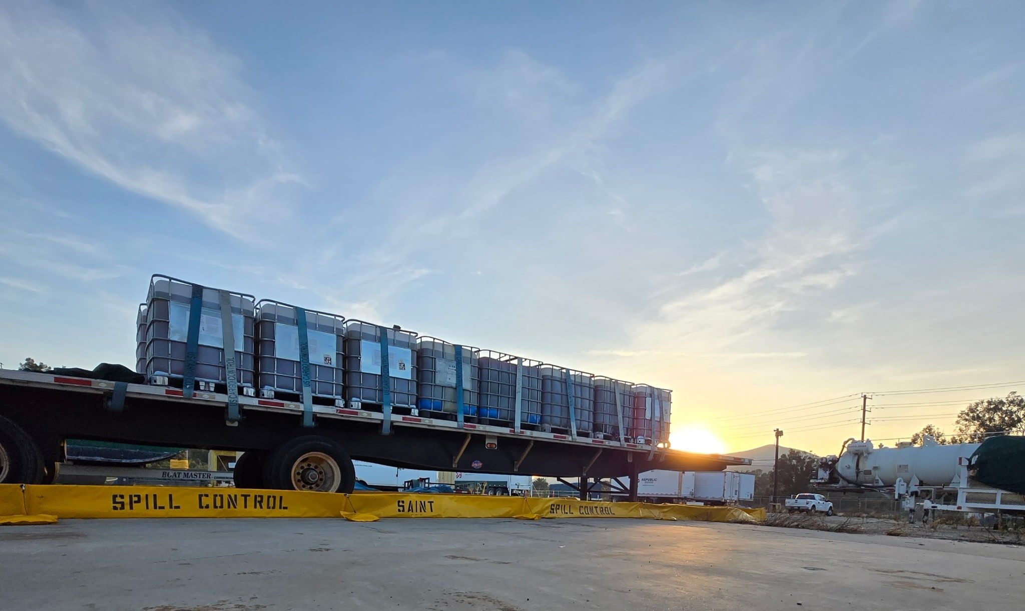 Long containment berm surrounding a flatbed trailer loaded with IBC totes at sunset