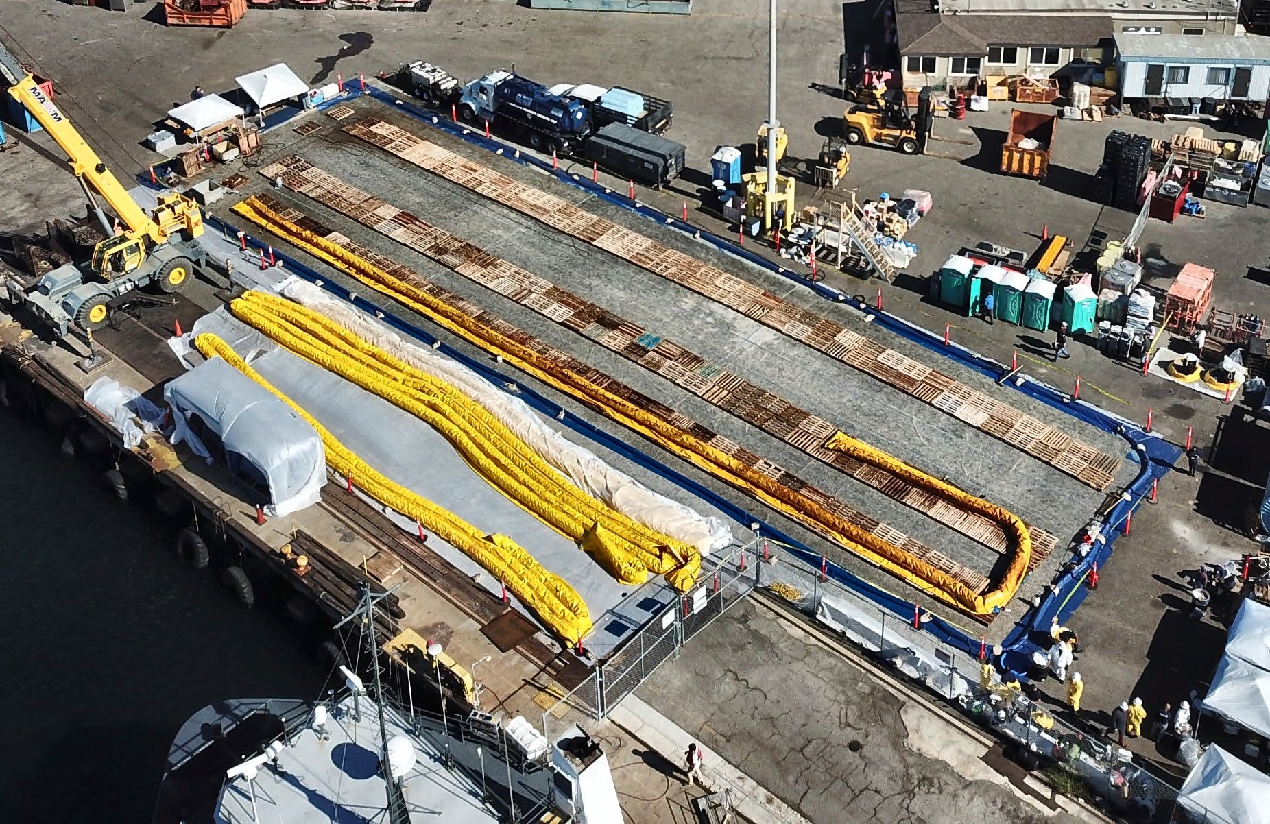 Aerial view of a dockside containment liner and staged oil containment boom along a working pier
