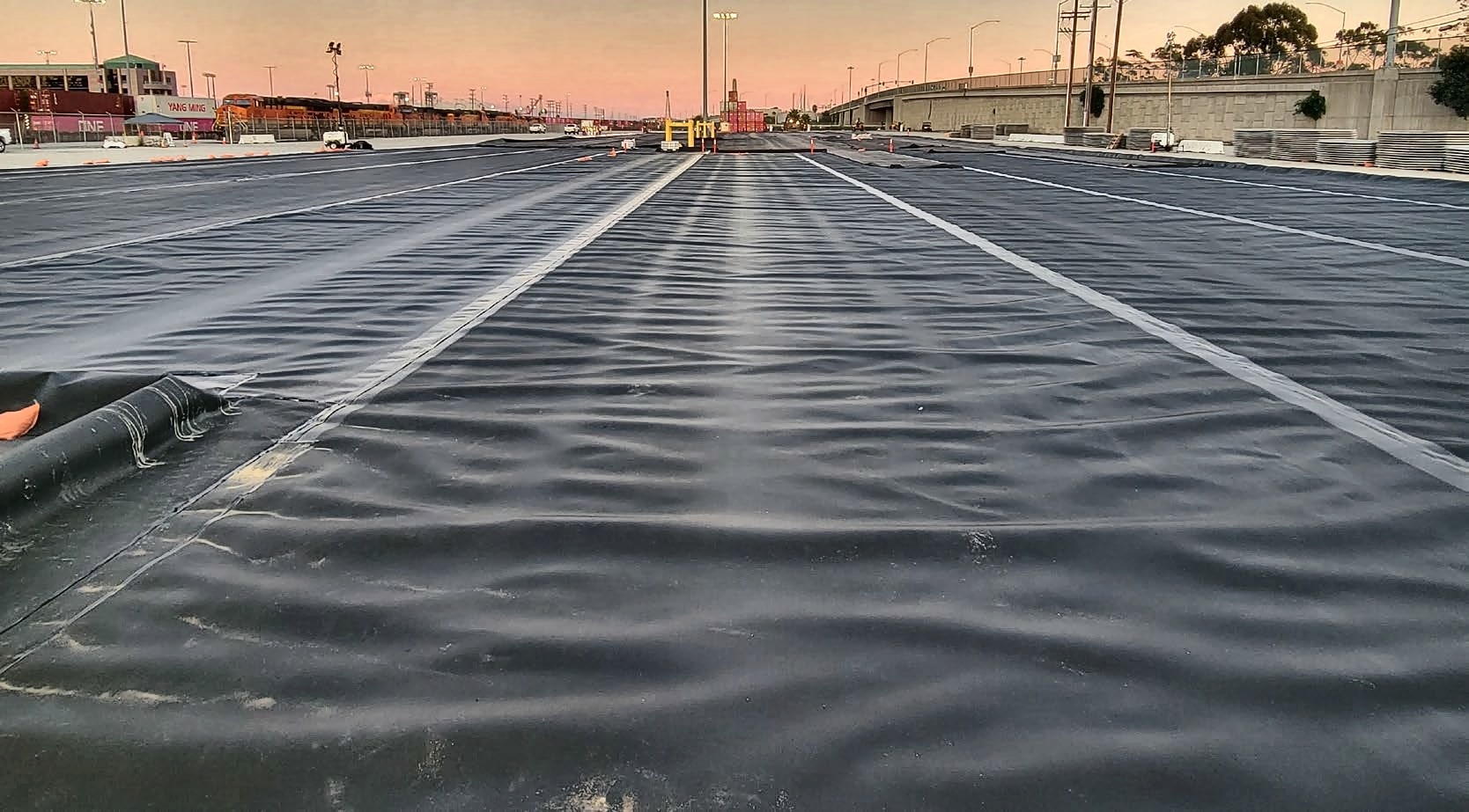 Large-area geomembrane containment liner installed across a port terminal yard at dusk