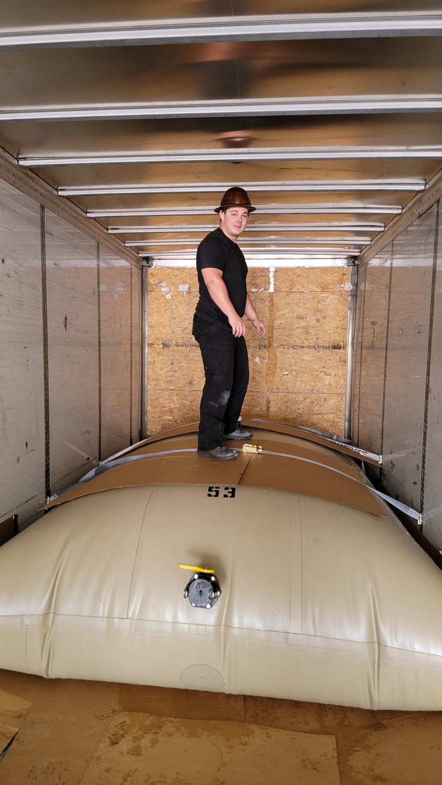 Worker in a hard hat standing on top of a filled transport flexitank inside a box trailer